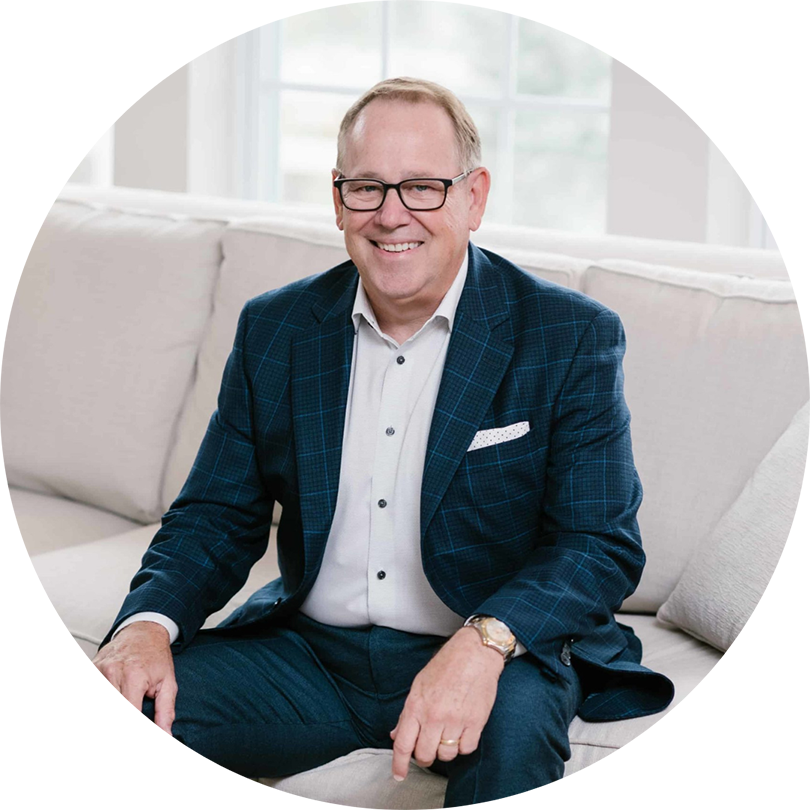 A round photo of Ed Chaffin in a blue andwhite tux sitting on a beige couch